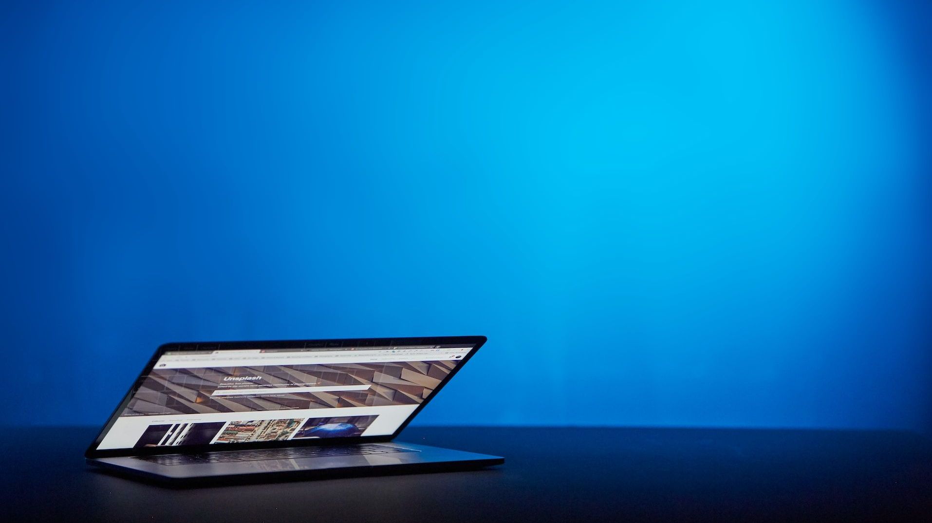 A laptop opens on a black table and dark blue background.